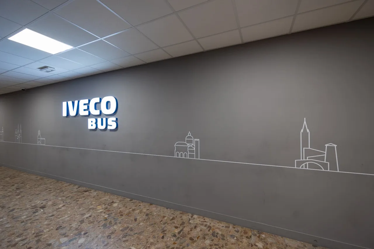 Šedá stěna s osvětleným logem IVECO BUS a linkovou grafikou